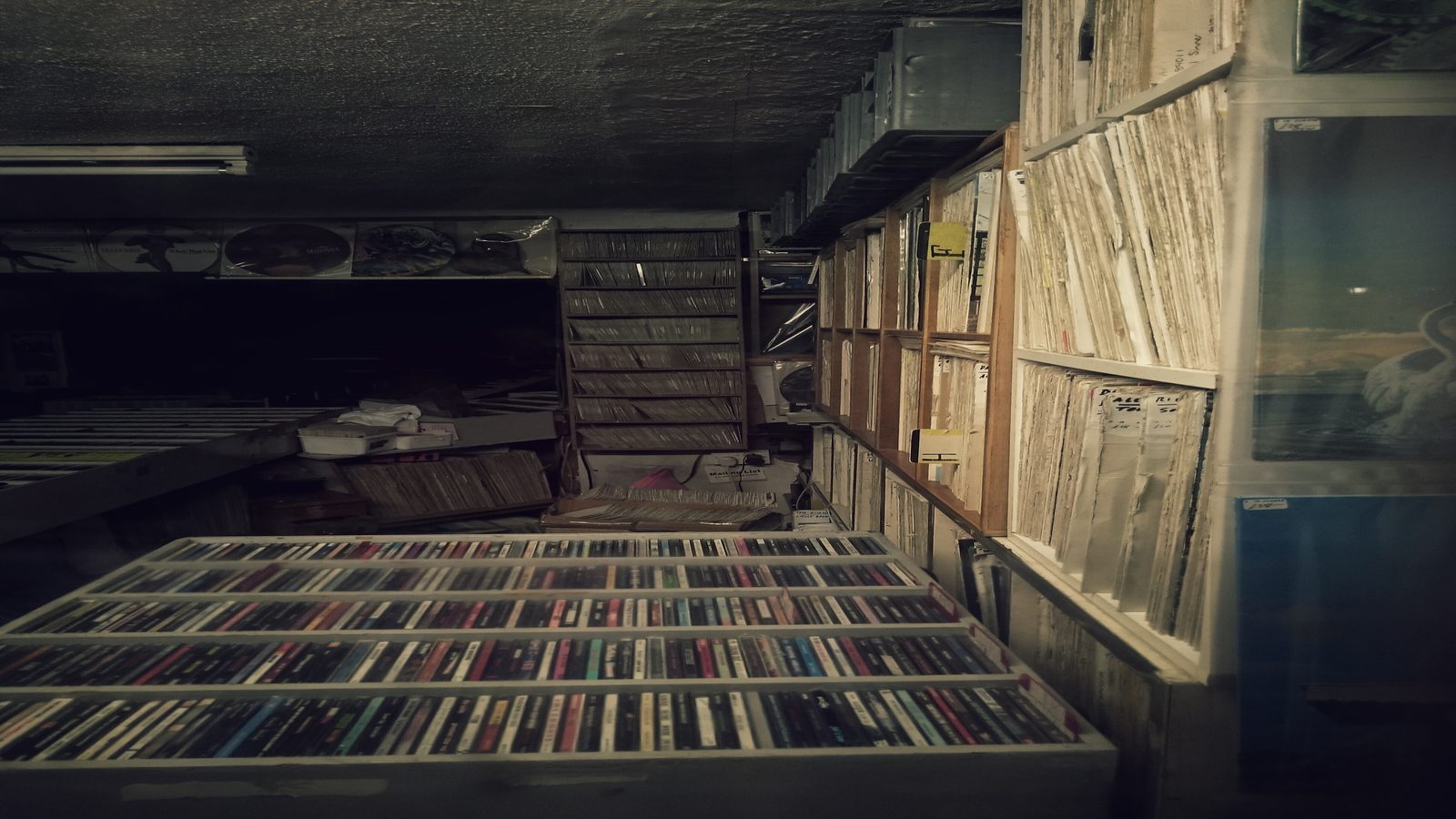 Stacked LP sleeves and a small notebook open to a list of records, on a paper-covered desk